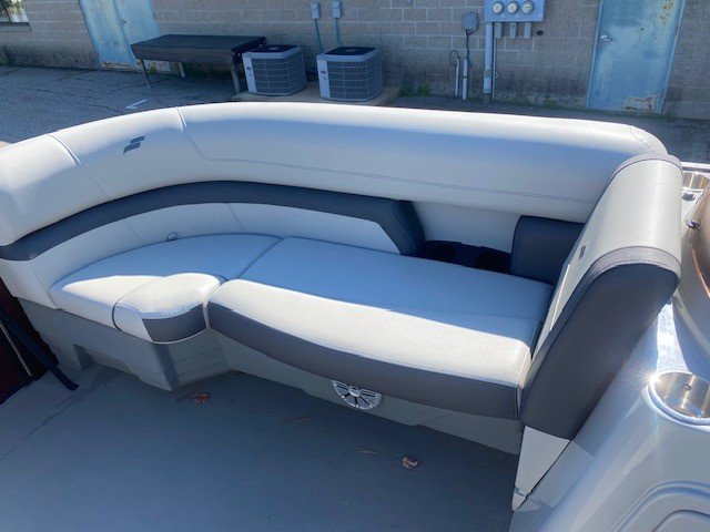 Interior view looking toward the stern of a Starcraft pontoon boat, featuring two light gray upholstered captain's chairs, a steering console, and additional rear lounge seating under a maroon bimini top.