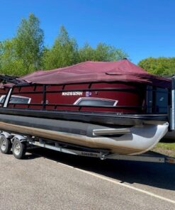 A maroon and black Starcraft pontoon boat with a matching maroon protective cover, sitting on a dual-axle LoadRite trailer parked on asphalt under a clear blue sky.
