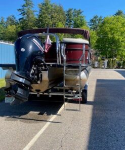 A maroon and black Starcraft pontoon boat with a matching maroon protective cover, sitting on a dual-axle LoadRite trailer parked on asphalt under a clear blue sky.