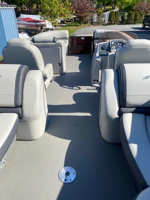 Interior view looking toward the stern of a Starcraft pontoon boat, featuring two light gray upholstered captain's chairs, a steering console, and additional rear lounge seating under a maroon bimini top.