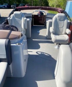Interior view looking toward the stern of a Starcraft pontoon boat, featuring two light gray upholstered captain's chairs, a steering console, and additional rear lounge seating under a maroon bimini top.