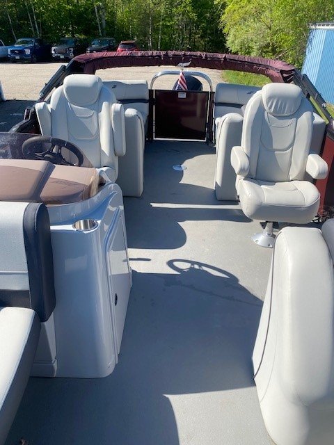 Interior view looking toward the stern of a Starcraft pontoon boat, featuring two light gray upholstered captain's chairs, a steering console, and additional rear lounge seating under a maroon bimini top.