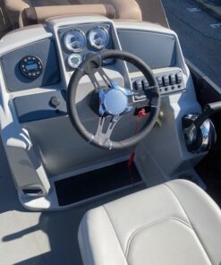 Interior view looking toward the stern of a Starcraft pontoon boat, featuring two light gray upholstered captain's chairs, a steering console, and additional rear lounge seating under a maroon bimini top.