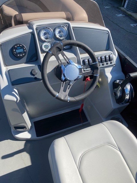 Interior view looking toward the stern of a Starcraft pontoon boat, featuring two light gray upholstered captain's chairs, a steering console, and additional rear lounge seating under a maroon bimini top.