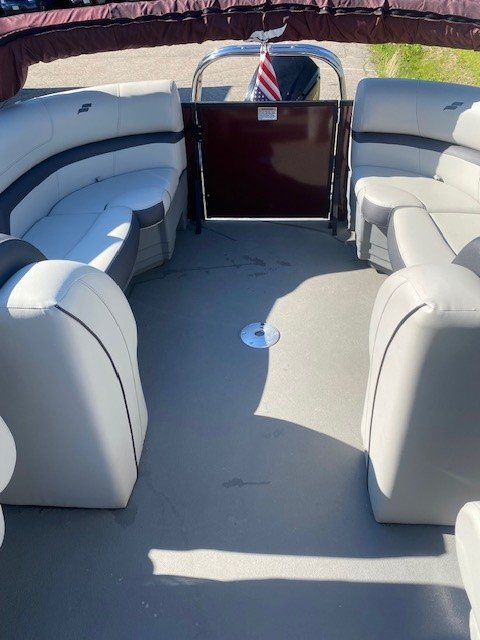 Interior view looking toward the stern of a Starcraft pontoon boat, featuring two light gray upholstered captain's chairs, a steering console, and additional rear lounge seating under a maroon bimini top.