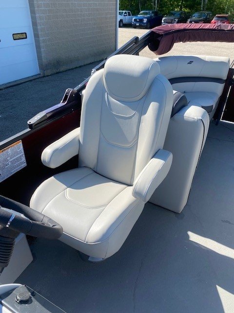 Interior view looking toward the stern of a Starcraft pontoon boat, featuring two light gray upholstered captain's chairs, a steering console, and additional rear lounge seating under a maroon bimini top.